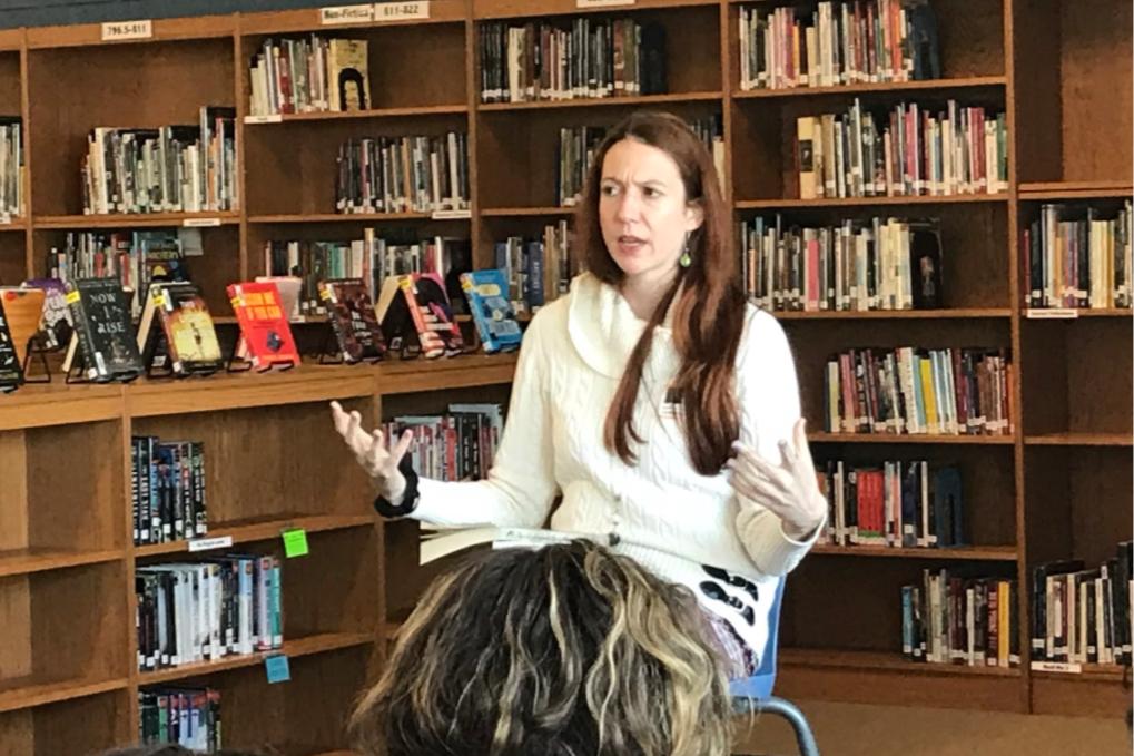 Person sitting in front of library bookshelves and talking