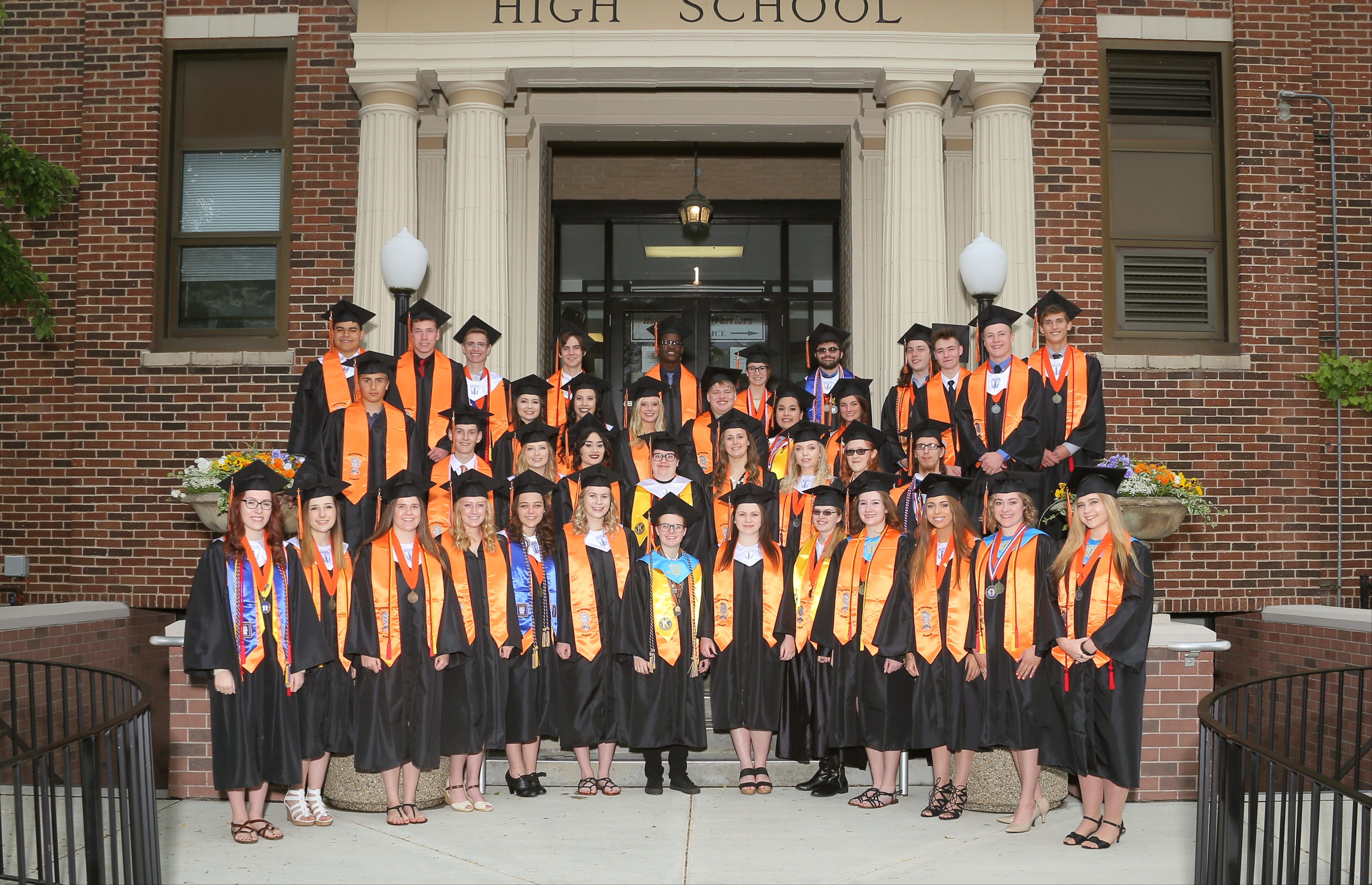 Class of 2017 East Campus Distinguished Warriors in stoles and graduation caps and gowns in front of East Campus