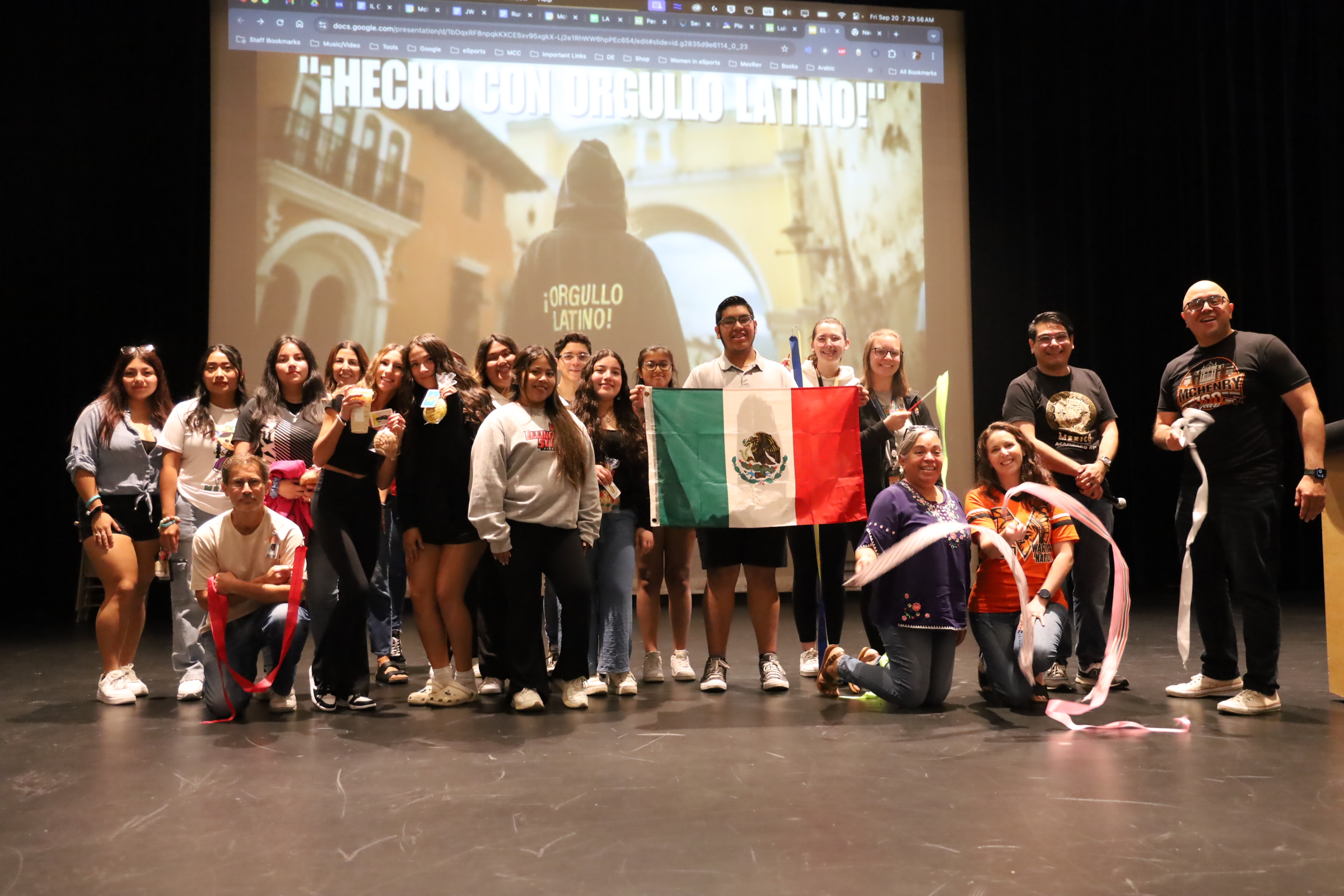 Students and staff posing with Mexican flag an da slide that says, "Hecho con orgulo Latino!" in the background.