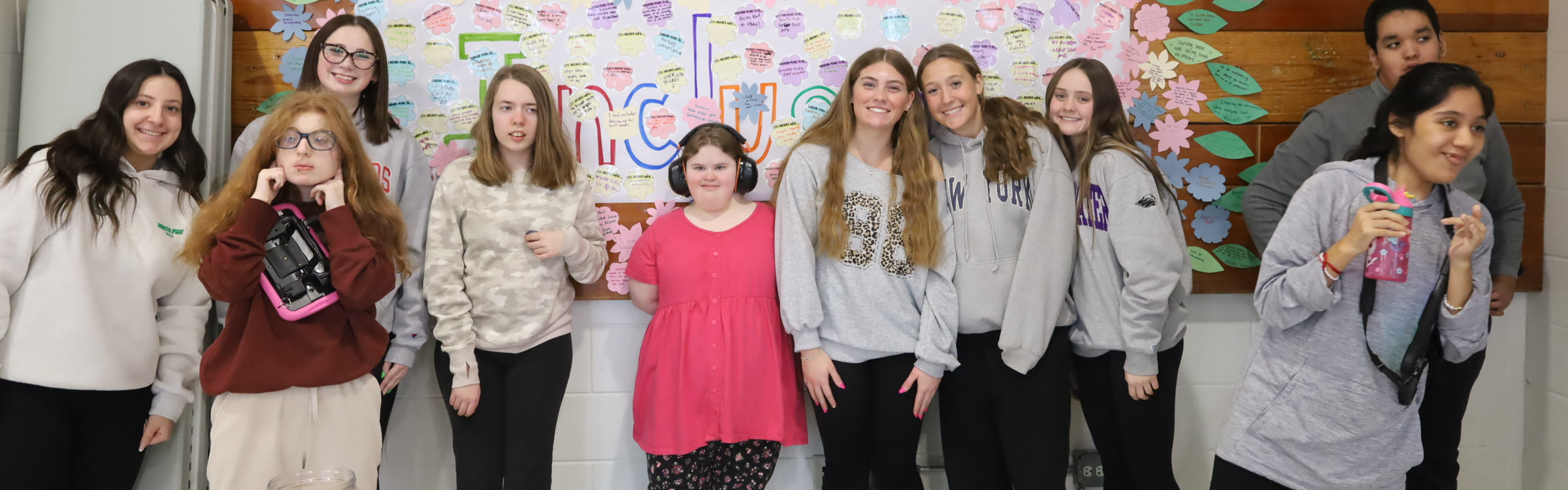 Students standing in front of inclusion wall with paper flowers and leaves