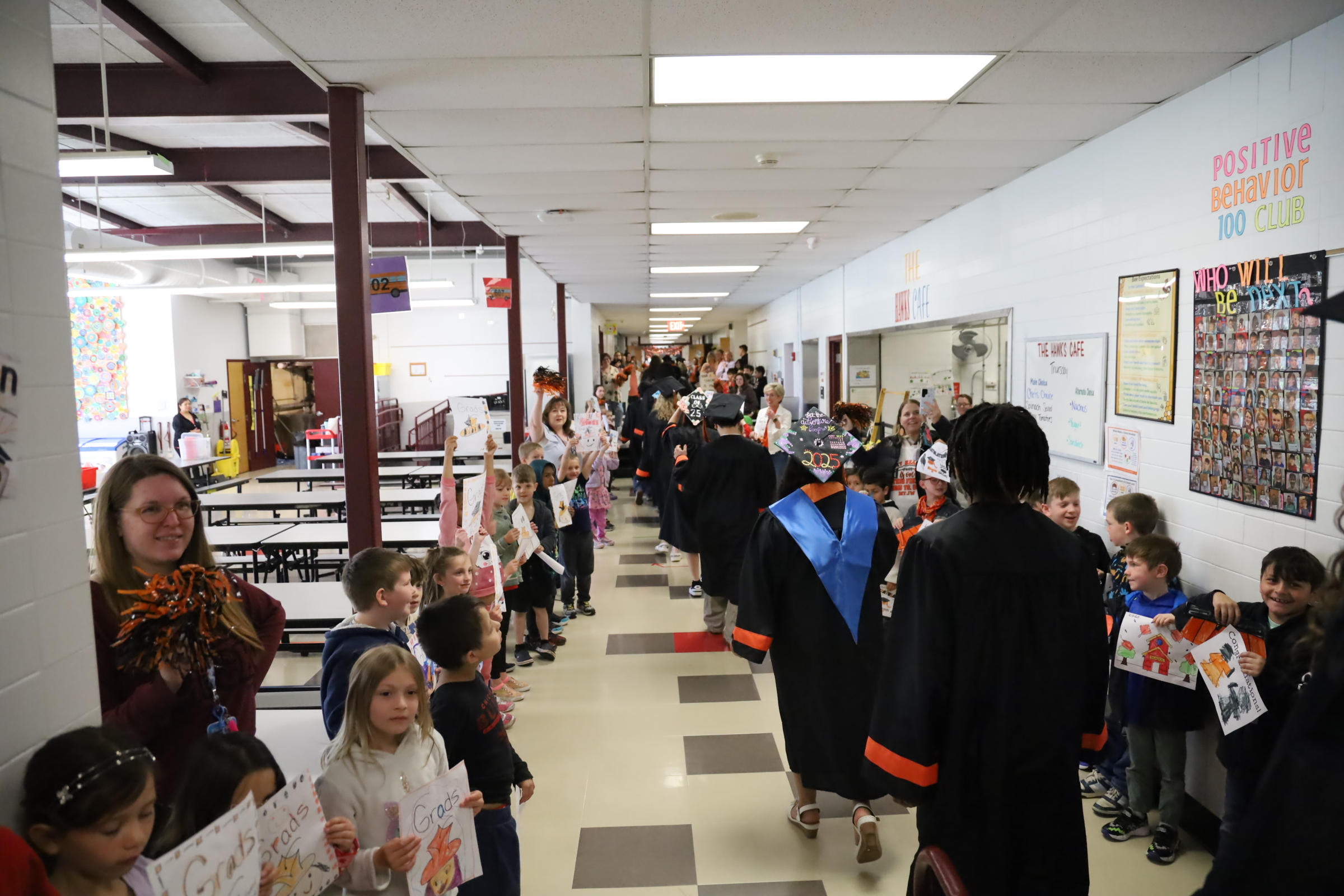 Students in graduation caps and gowns walking with elementary school students cheering for them 