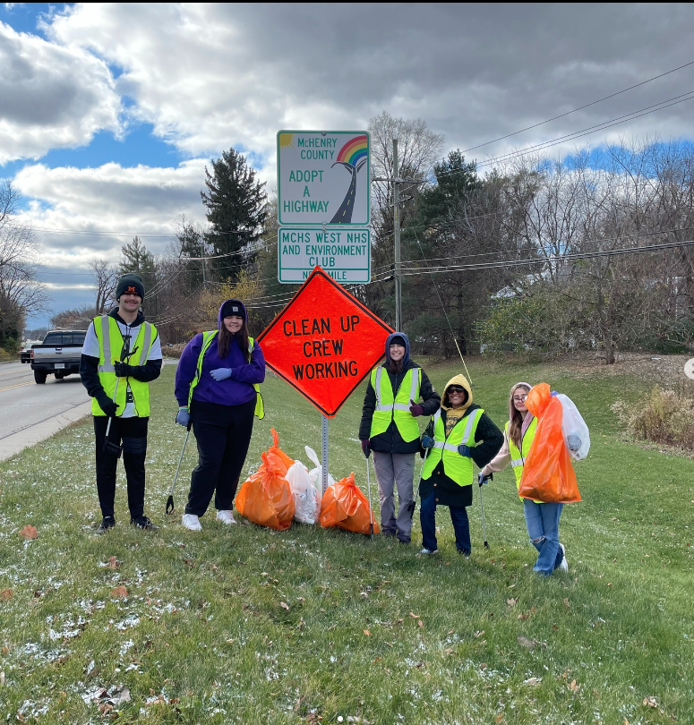 Students cleaning up trash on the side of the road with Clean Up Crew woring orange sign