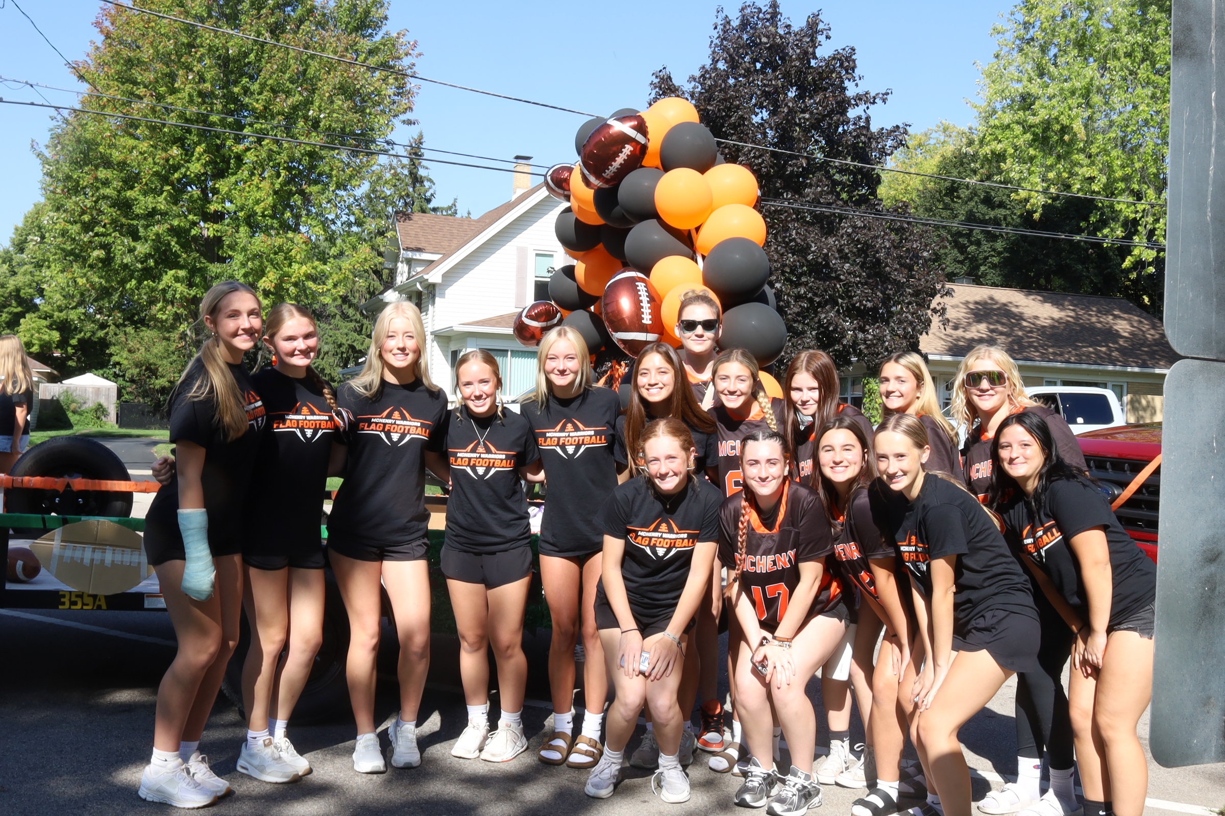 Flag football team posing in front of their float with orange and black balloon arch and football