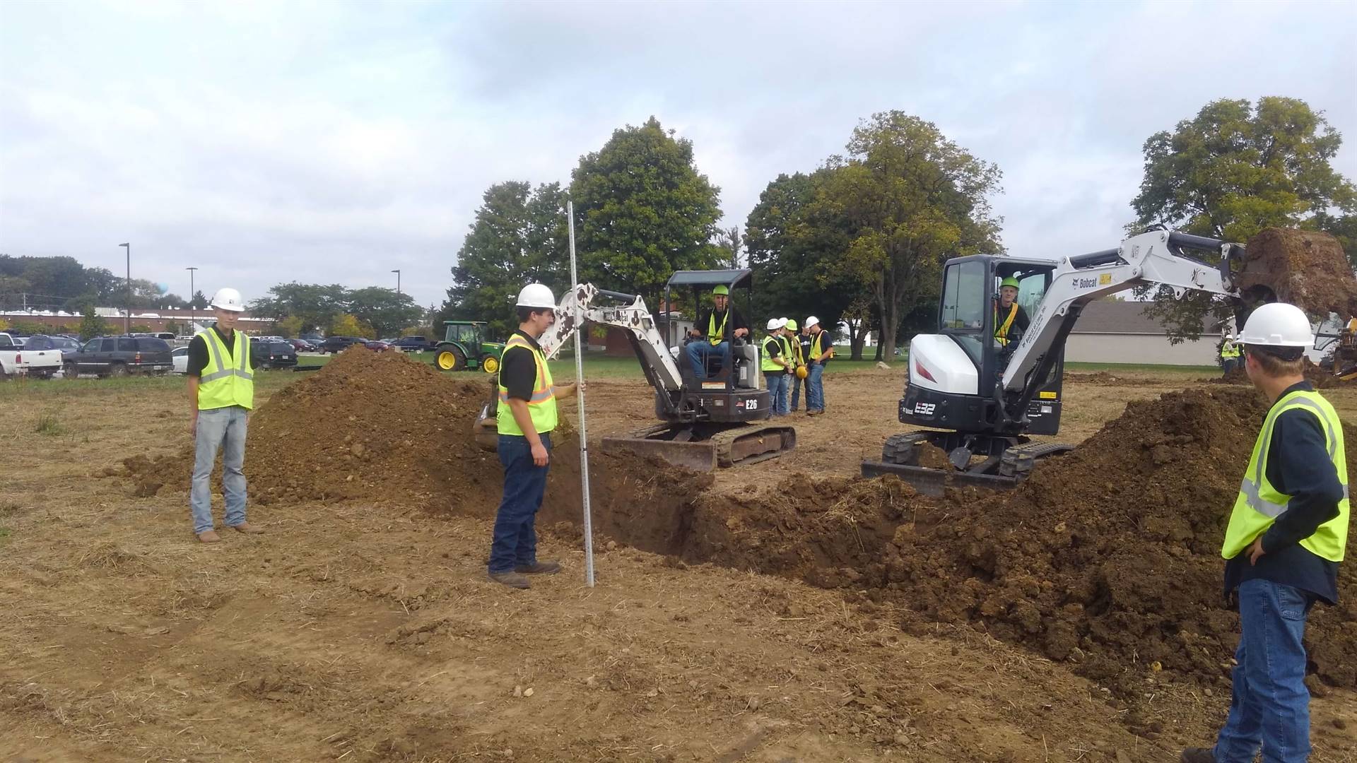 Students supervising other students digging with excavators
