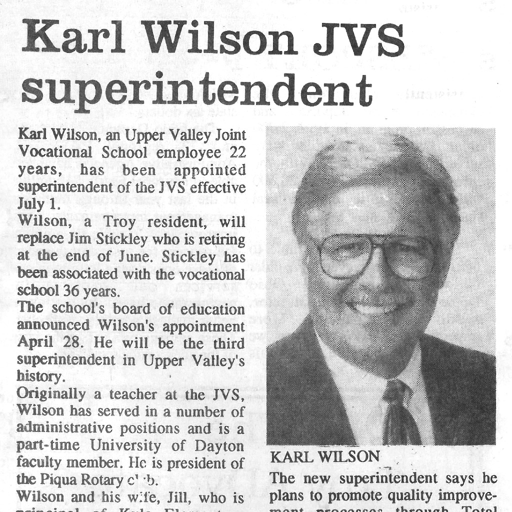 A vintage newspaper clipping from 1997 announces Karl Wilson as the new superintendent. The image features a man smiling in a suit and glasses.