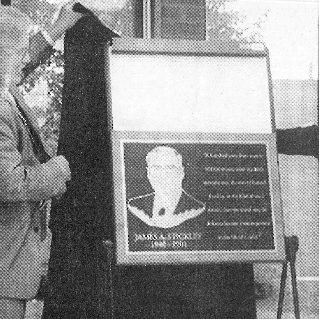 Black-and-white photo of two people revealing a plaque in 2002. The plaque is dedicated to a former superintendent.