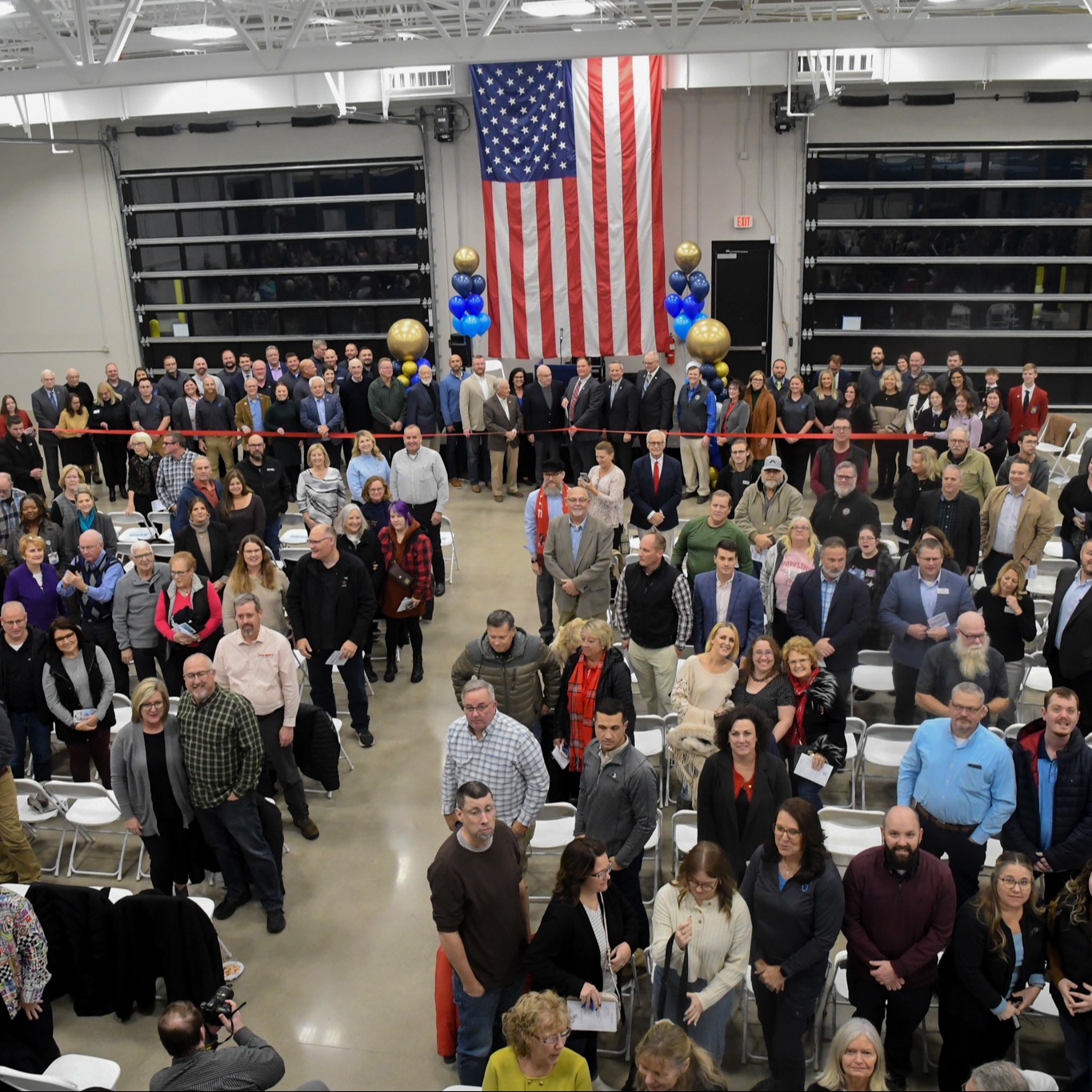 A large group of people gathered in a hall, with tables and chairs, for an event.