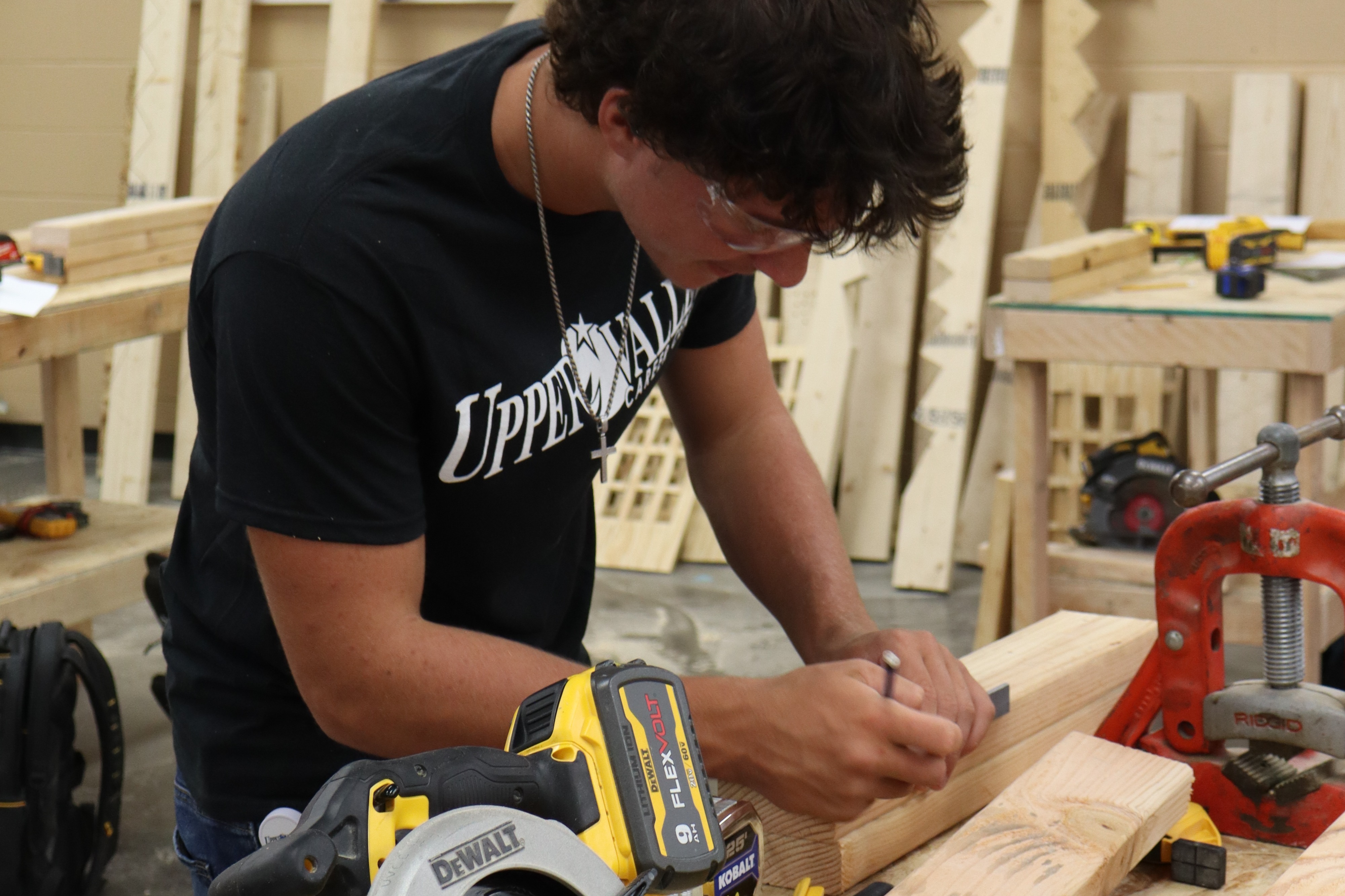 A person wearing a black shirt and glasses uses a circular saw to cut a piece of wood.