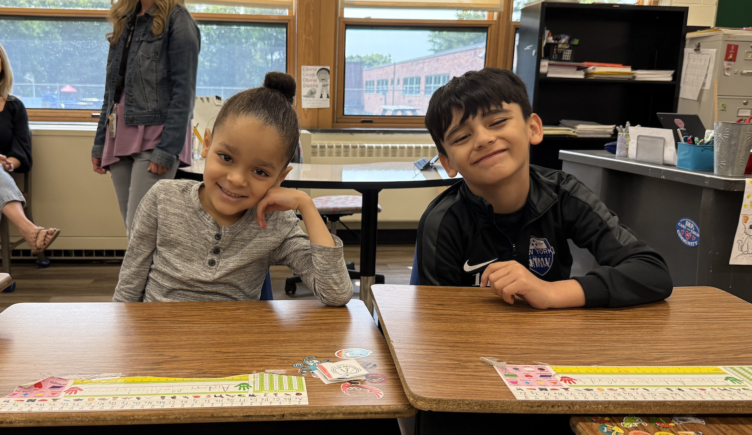 two students wearing grey and black sweatshirts sitting at brown table
