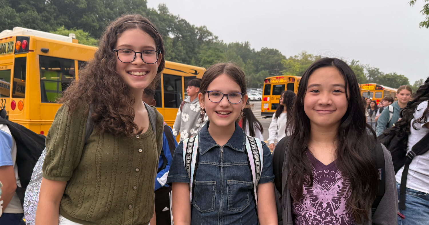 three students with backpacks in front of school bus 
