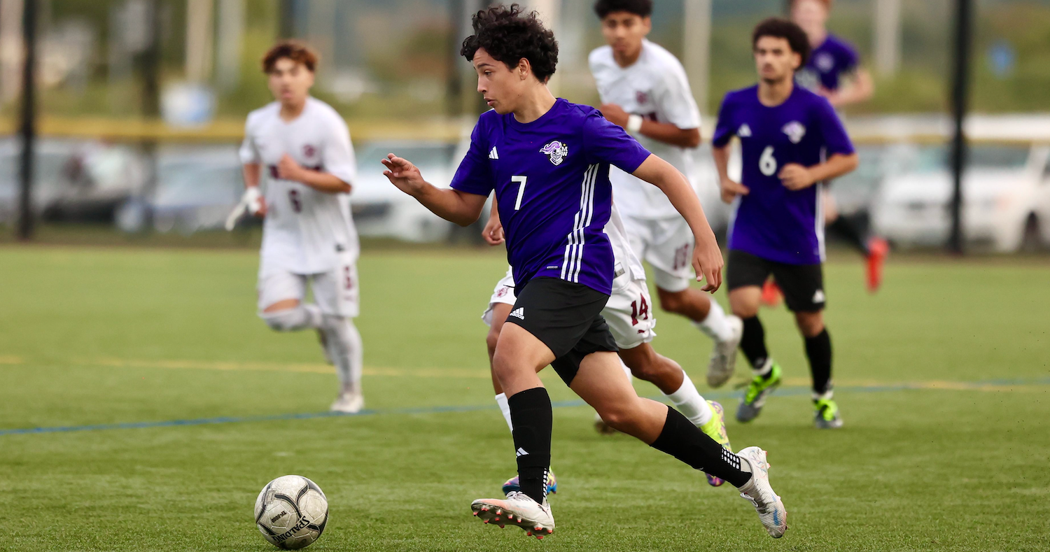 Student in purple jersey kicking a soccer ball