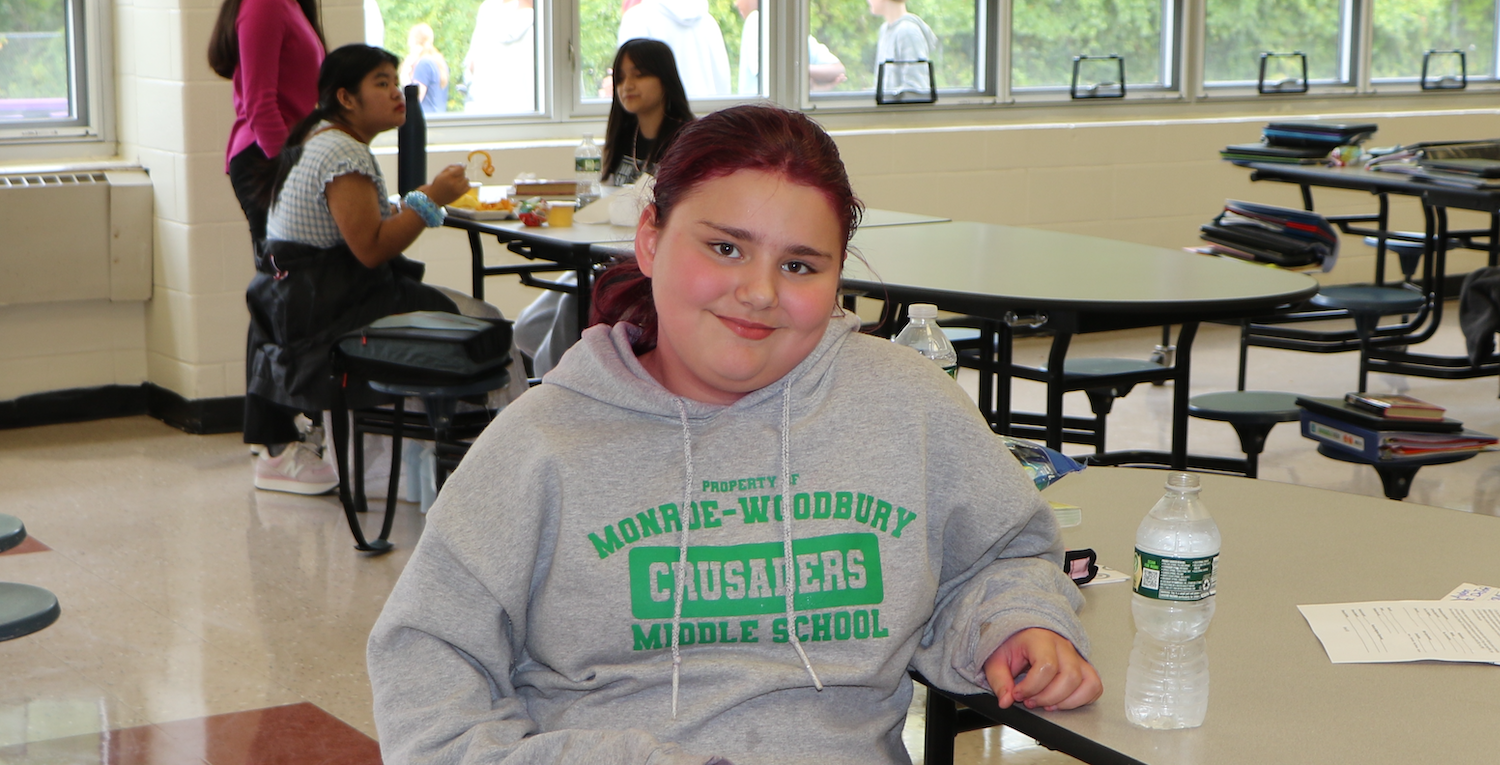 student wearing a grey sweatshirt with green letters sitting at lunch table