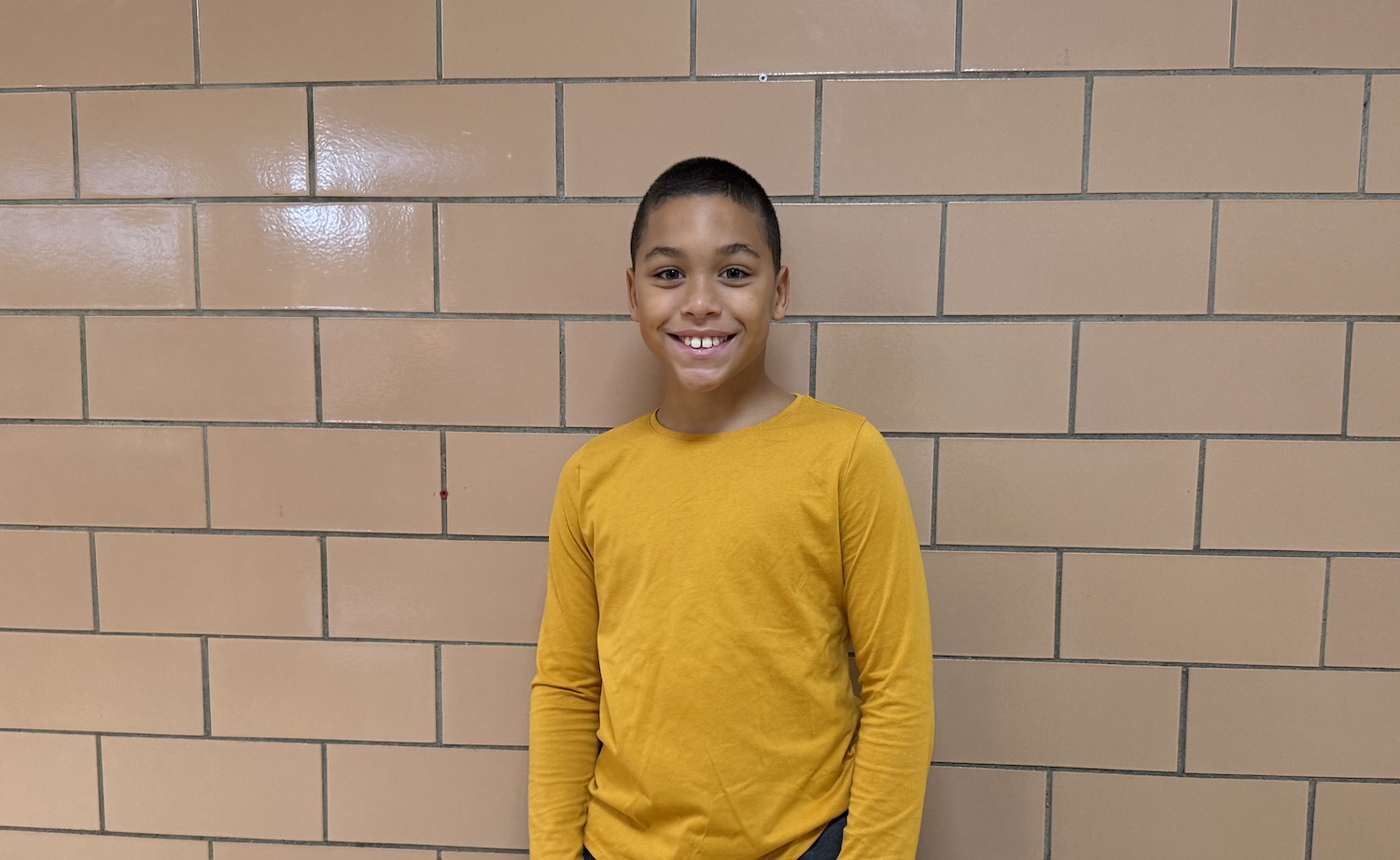 student wearing a gold shirt standing in a brown hallway