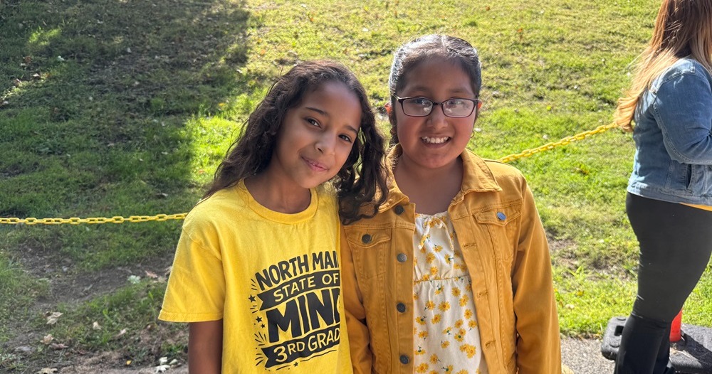 Two girls in a park with a yellow rope, one in a yellow shirt and the other in a yellow jacket.