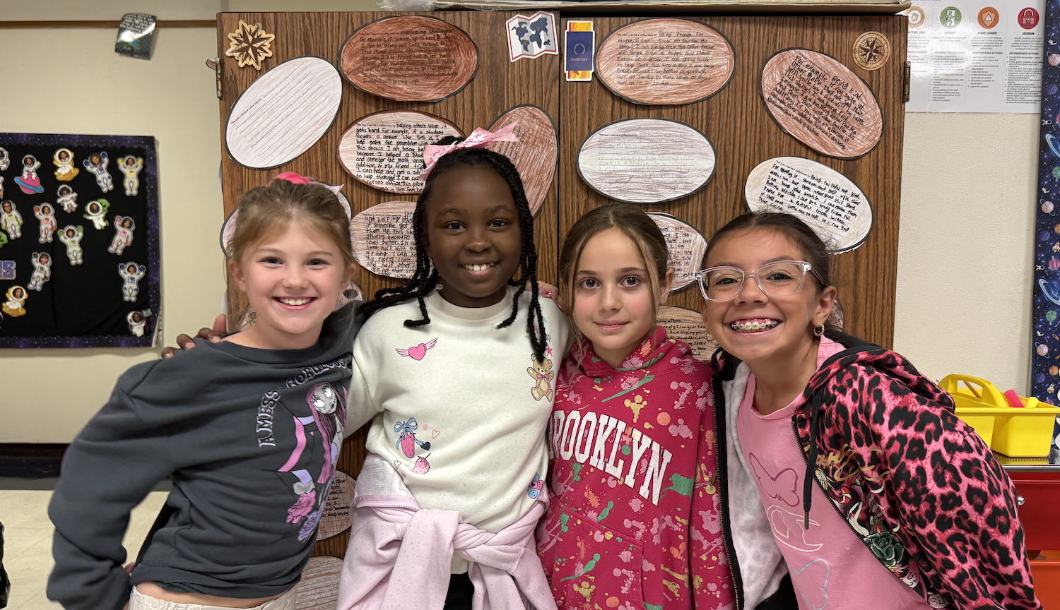 Four young girls pose for a picture in front of a wall with various paper circles.