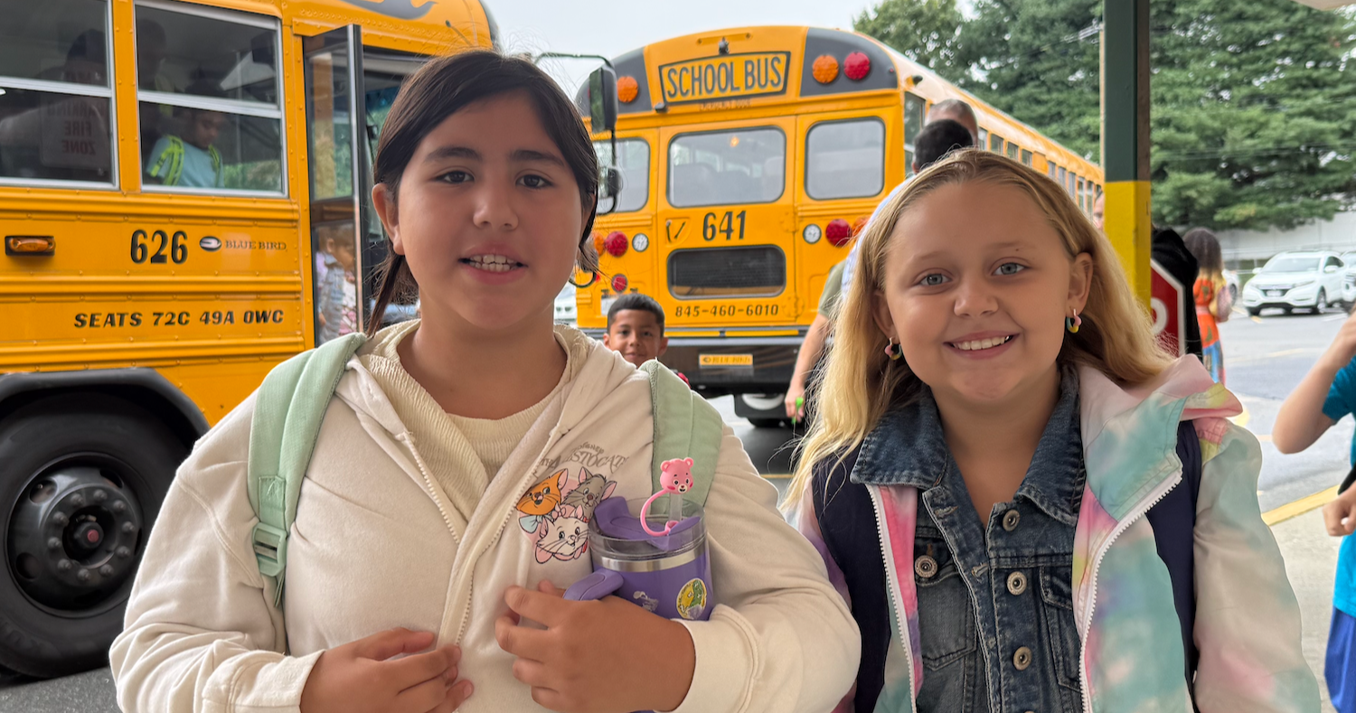 two students standing front of school buses
