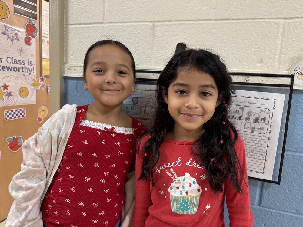 Two young girls smiling, one in red with white accents, the other in red with a cupcake graphic.
