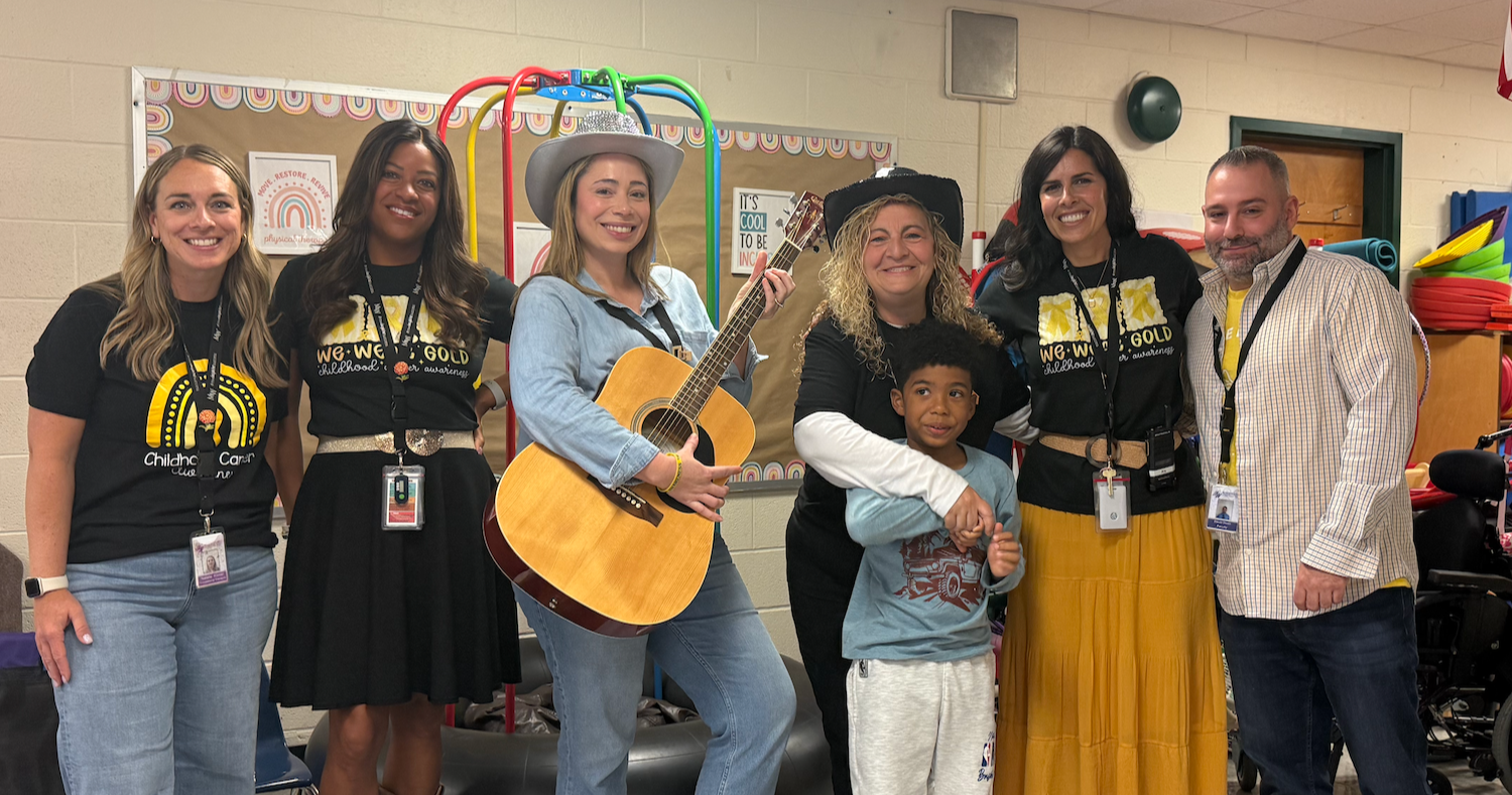 Seven adults and one child in a classroom pose for a photo. One adult holds a guitar.