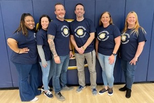 Collingswod High School counseling staff posed in the school gym, smiling, happy to represent the school. Everyone is wearing matching Collingswood logo shirts. 