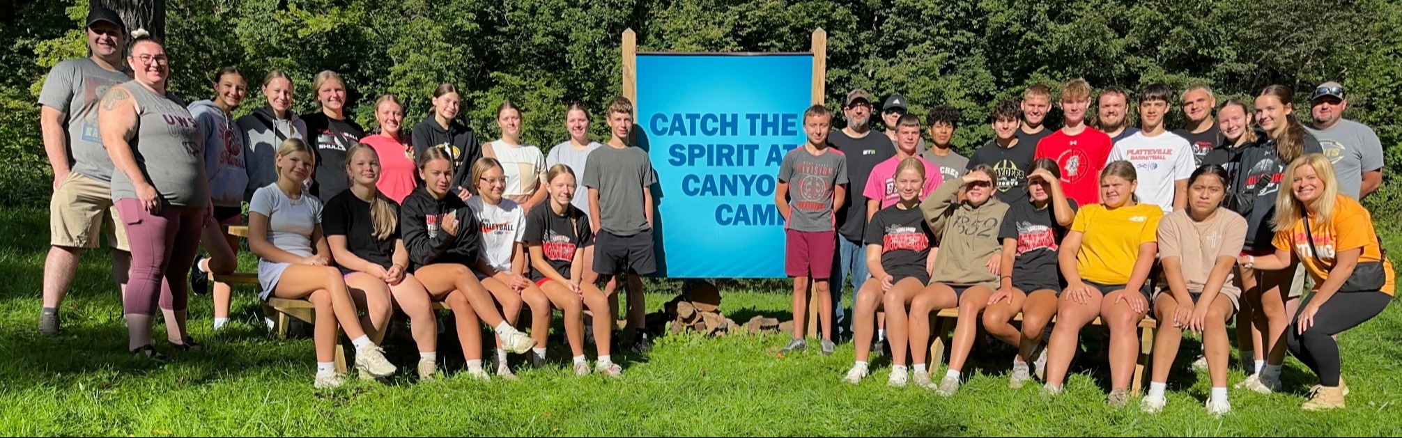 A large group of people poses for a photo in a park with a banner behind them.