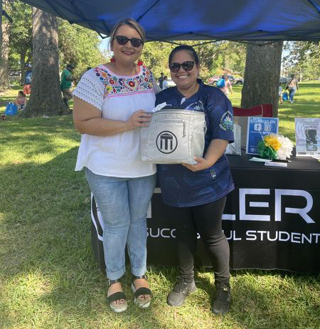 two women stand next to each other holding a Tyler ISD bag
