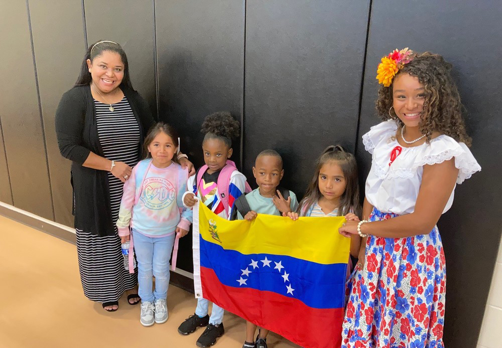 two women stand with four elementary aged children between them holding the Venezuela flag