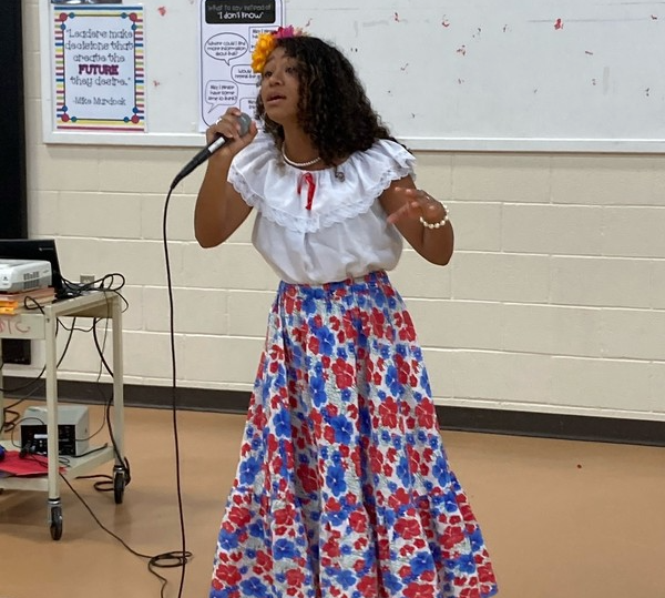 woman wearing white shirt and floral skirt sings with microphone