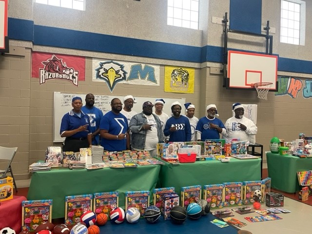 African American college age men standing behind tables full of toys and books