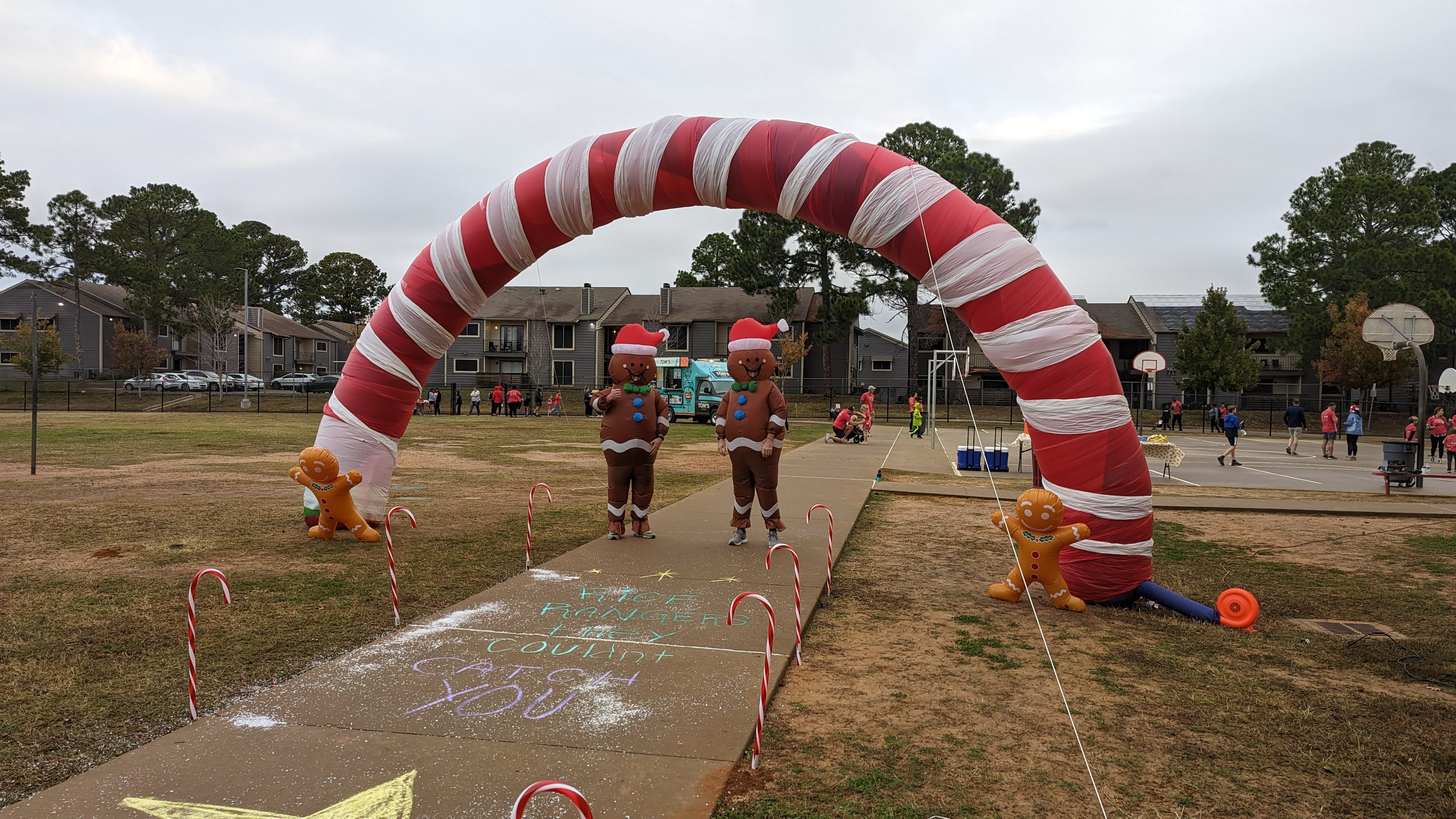 two inflatable gingerbread figures run on sidewalk under a candy cane arch