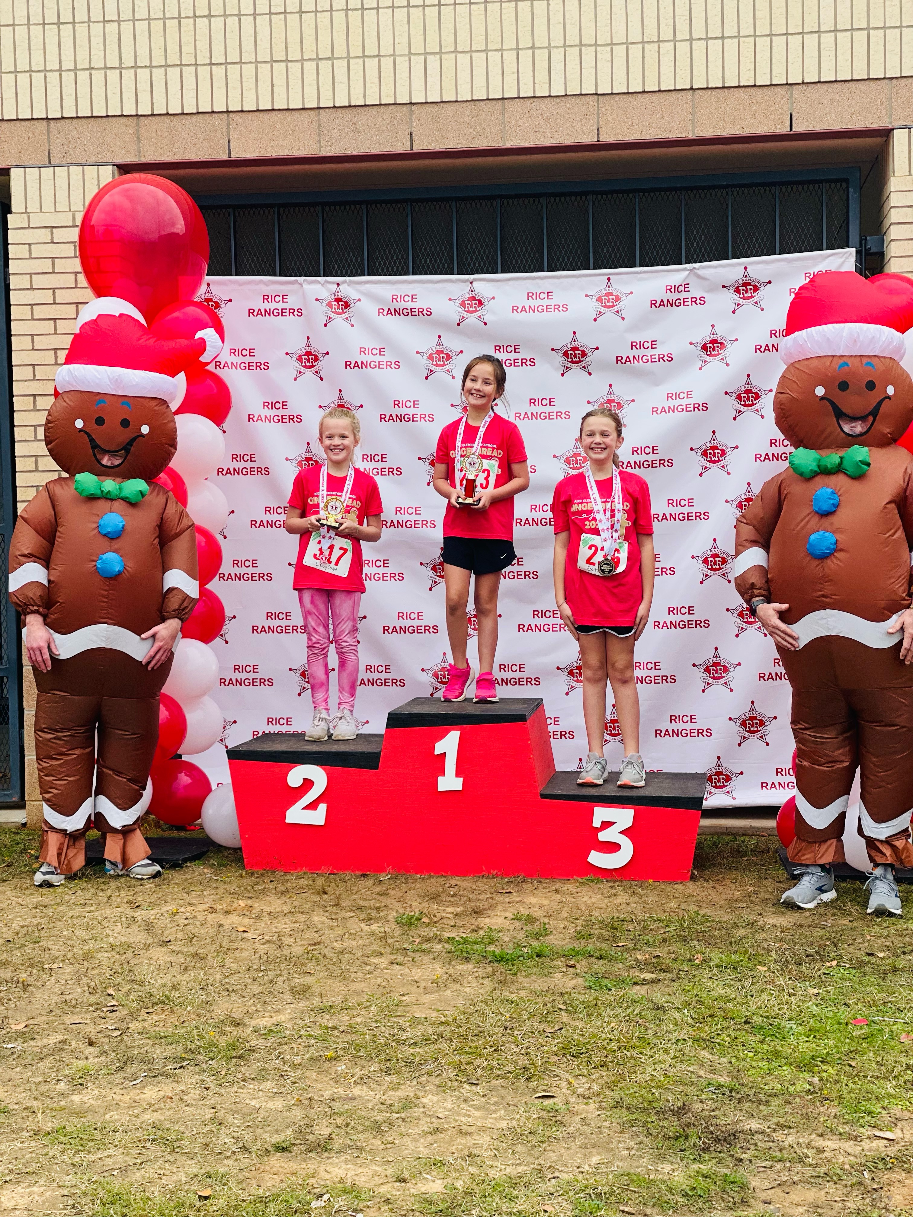 elementary age students standing on a winners stage with inflated gingerbread figures on each side