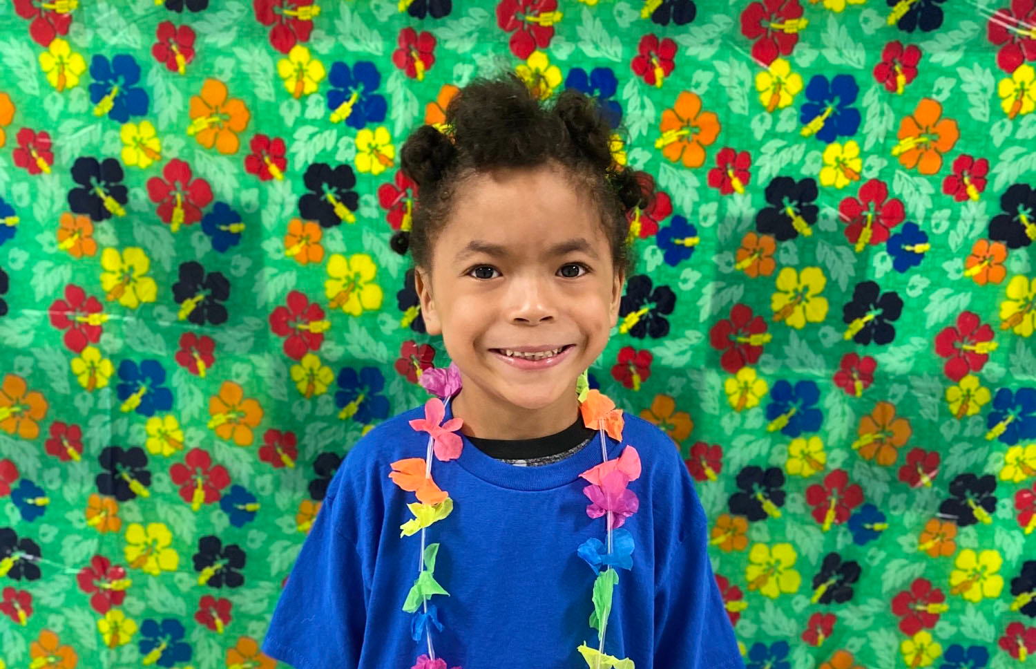 elementary age child wearing a blue shirt and Hawaiian lei smiles at the camer