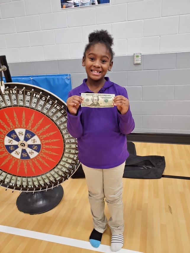 elementary aged African American girl holding a $20 bill next to a wheel she spun to see her prize