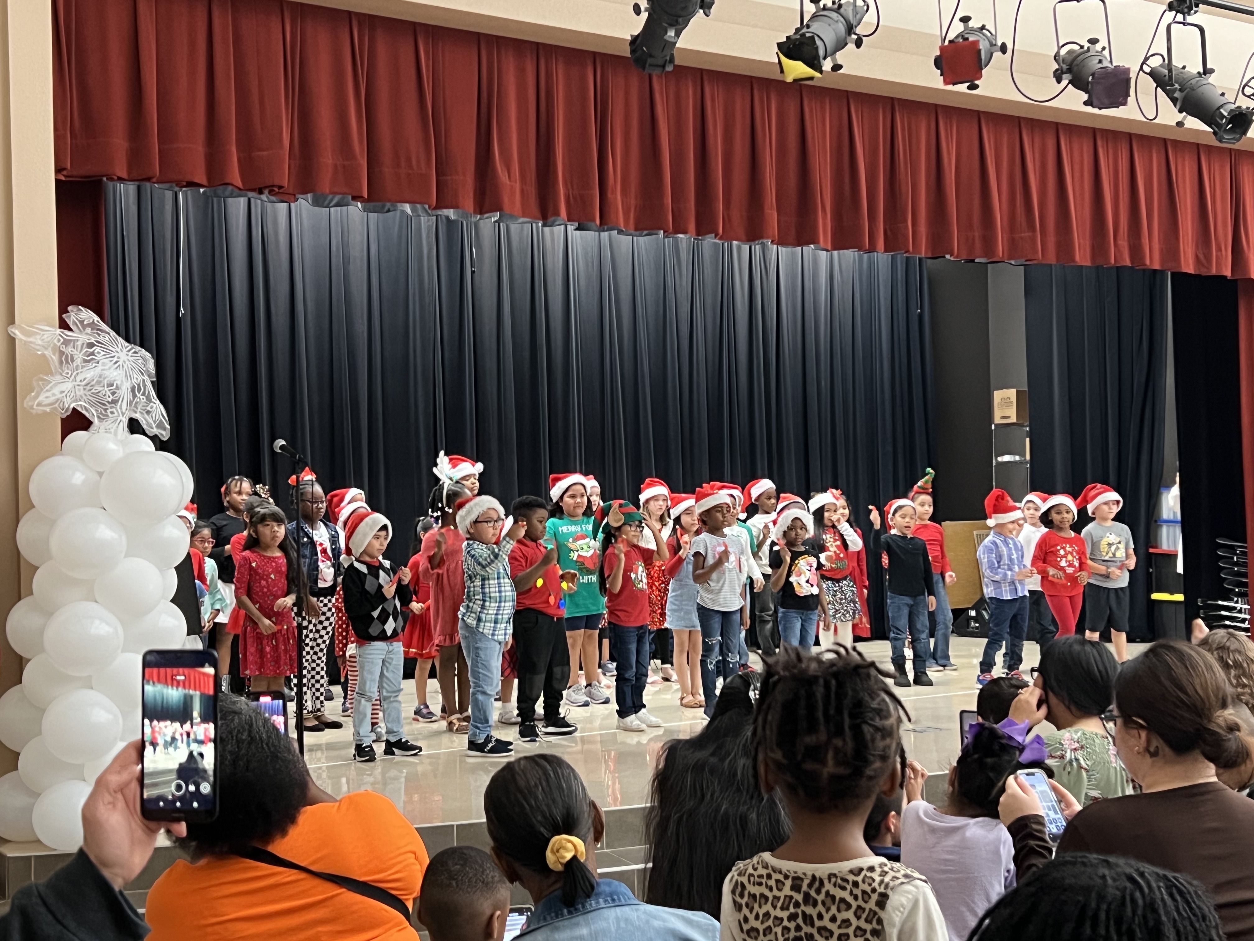 elementary aged students perform on stage wearing Santa hats