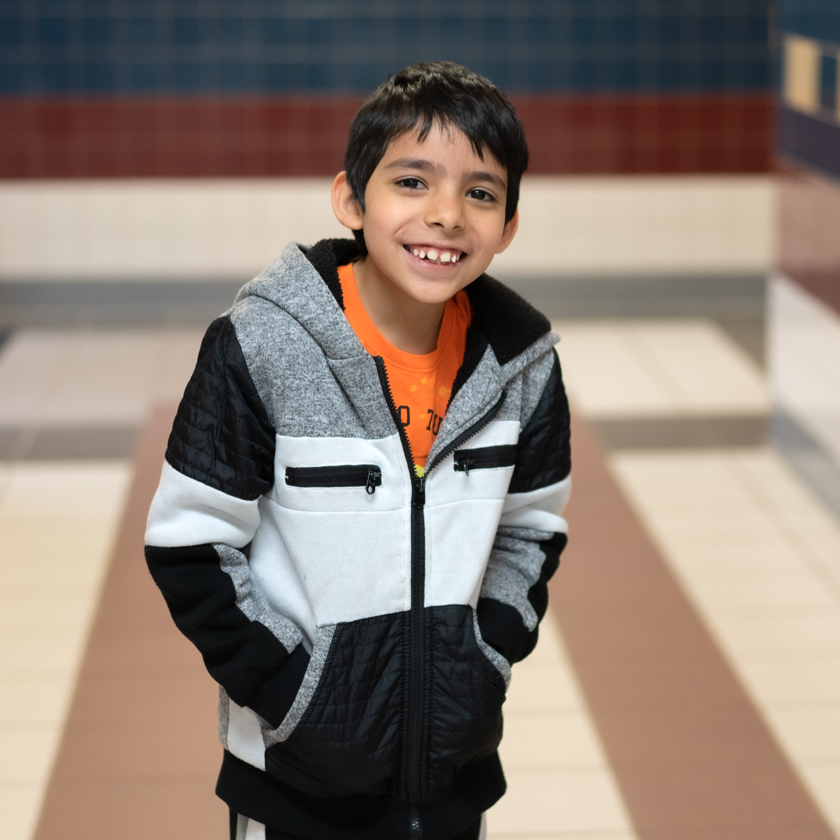 elementary age Hispanic boy wearing a black, white and gray jacket