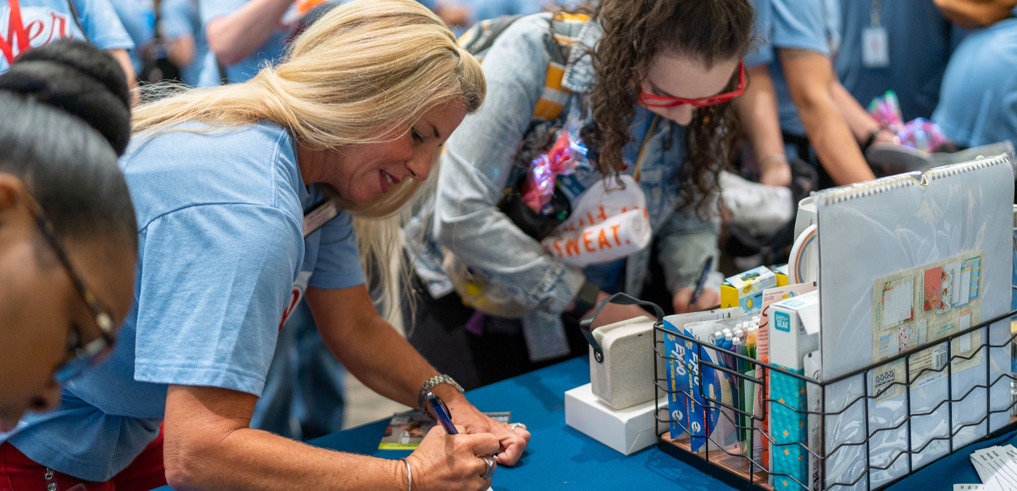 women wearing blue tshirts lean over a table signing cards
