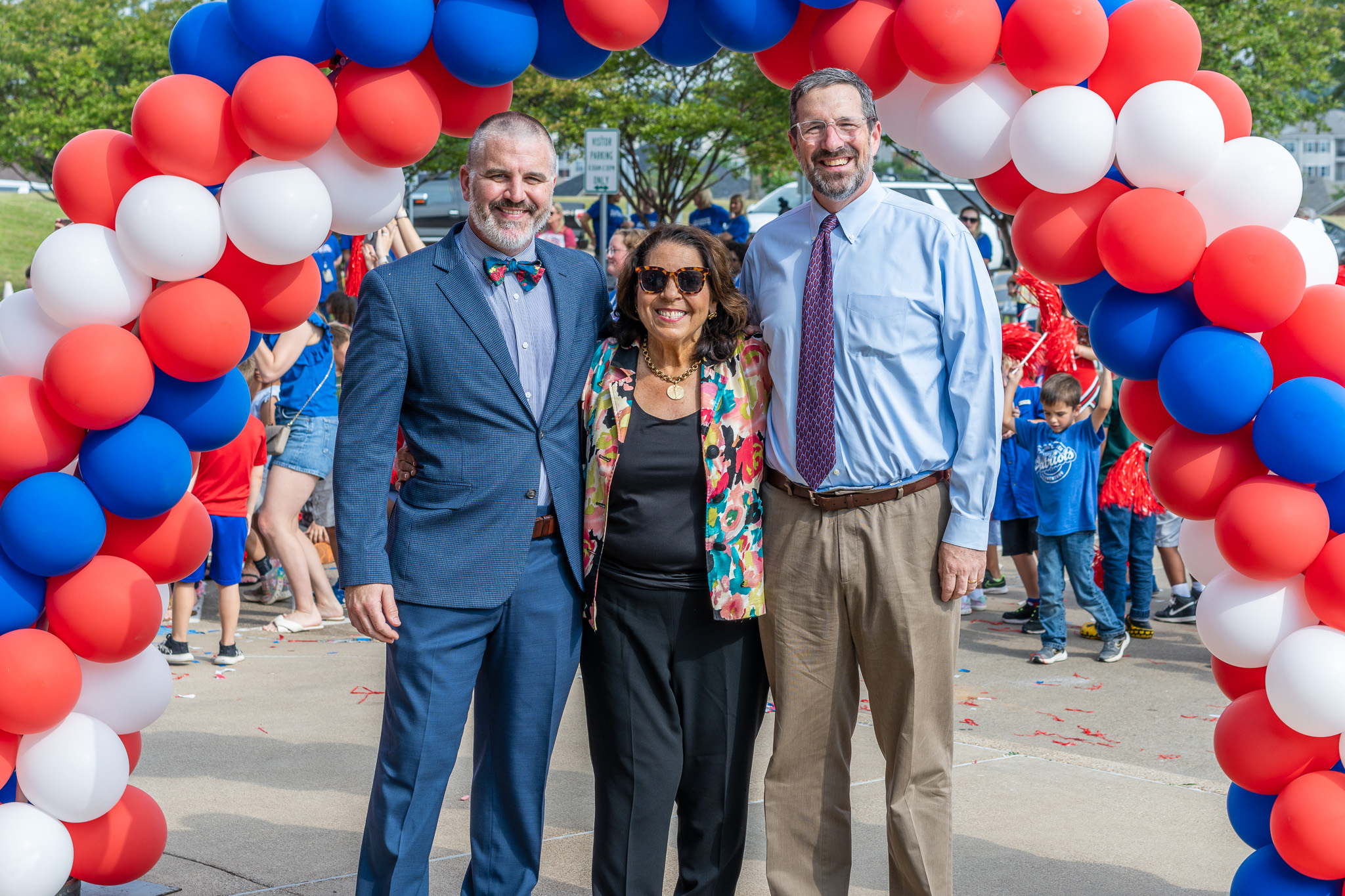 two men and a woman stand under a balloon arch