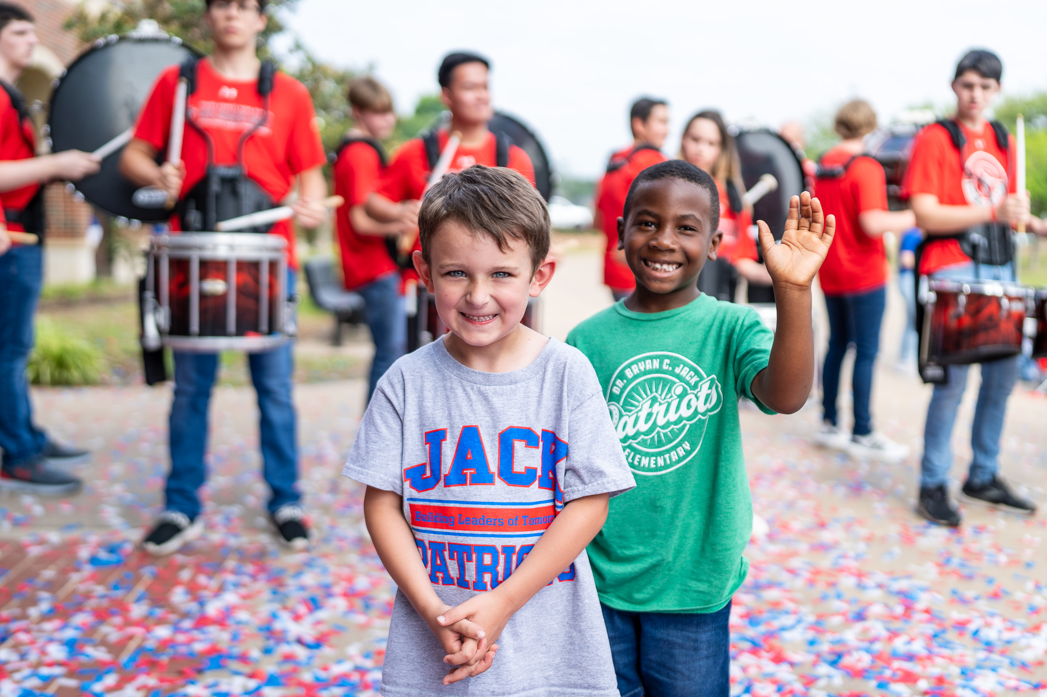 two elementary age boys stand in front of the high school drummers with confetti all over the ground