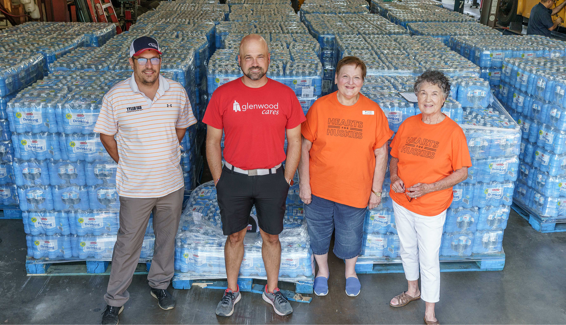 two men and two women standing in front of pallets of water