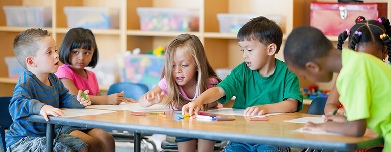 young children sitting at a table, coloring pictures