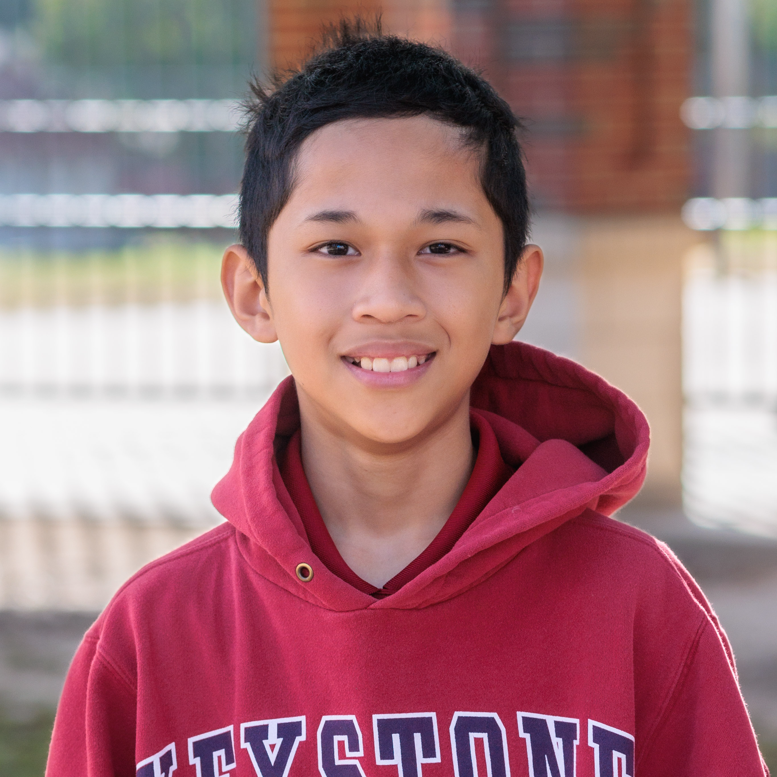 Asian elementary age boy wearing a red hoodie standing outside his school