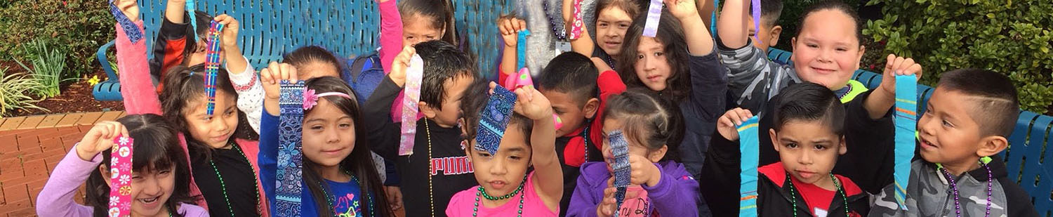 young children of various ethnicities holding pieces of ribbon in the air
