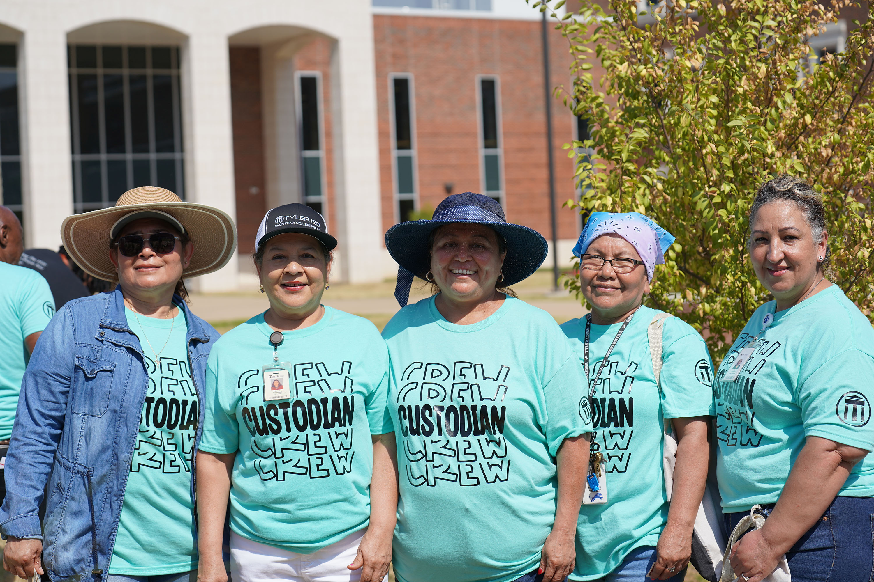 women wearing teal green t-shirts stand in front of a school