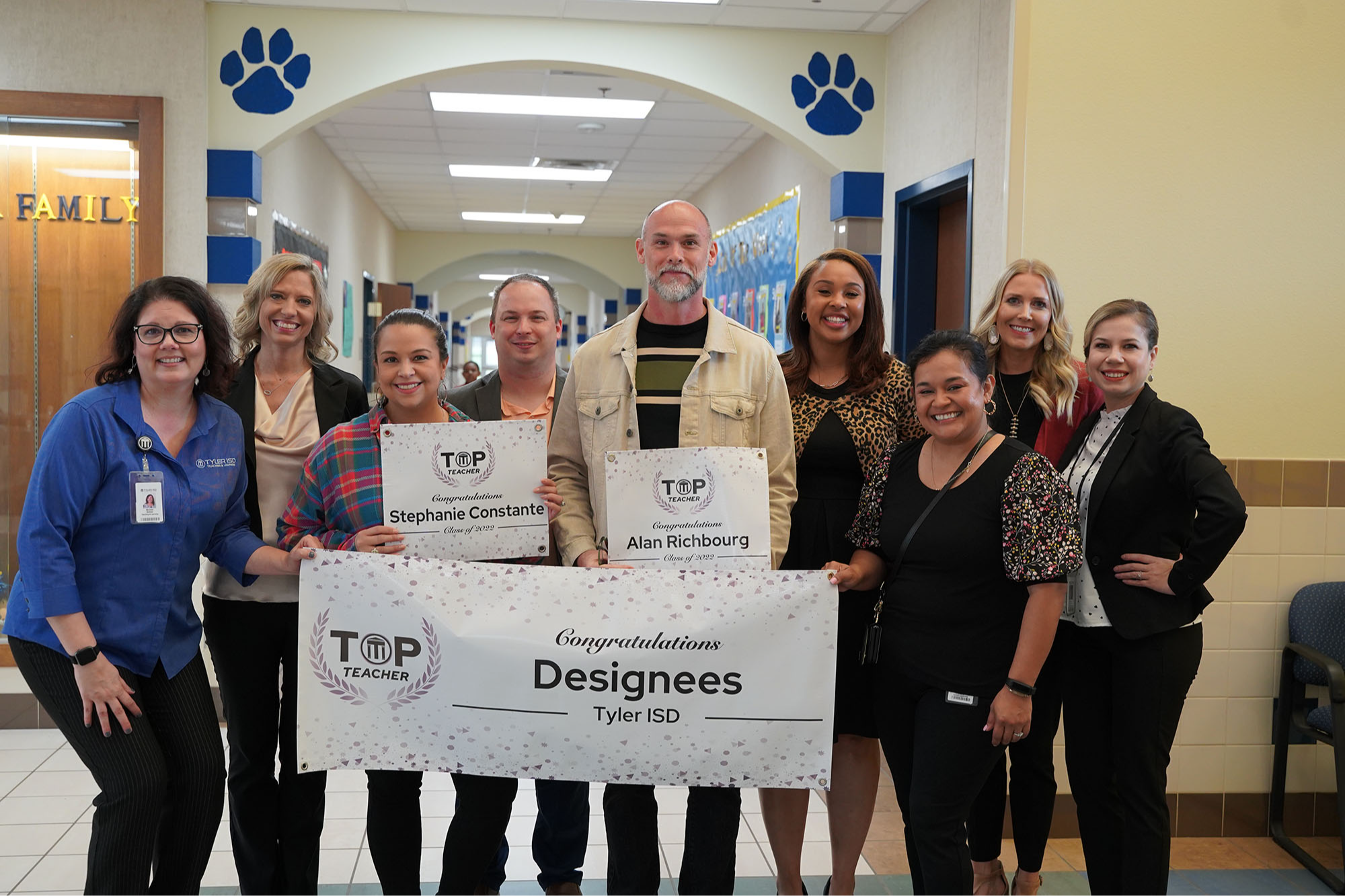 group of men and women standing behind a banner that says, "TOP Teacher - Congratulations Designees Tyler ISD"