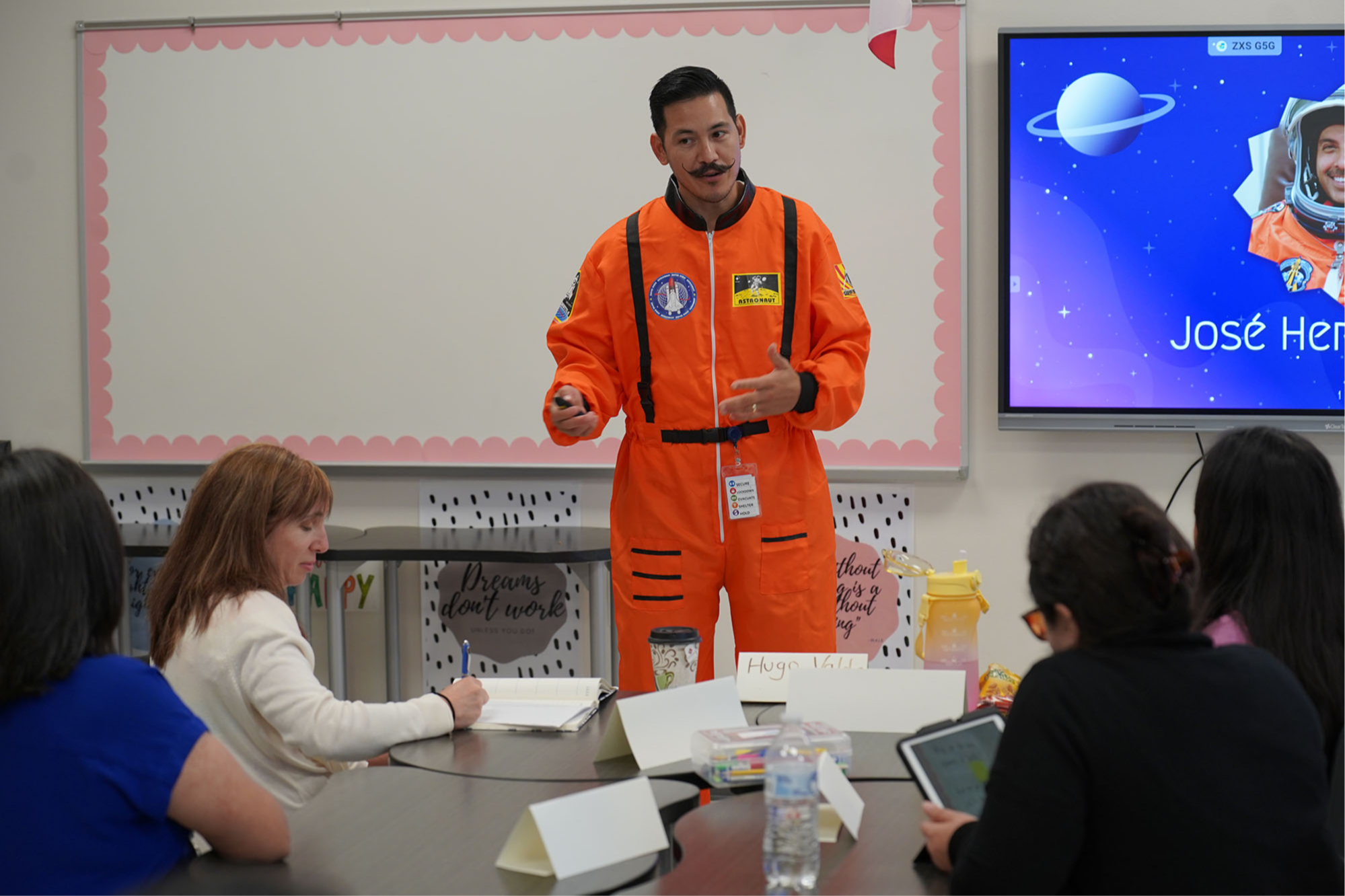 man dressed in orange astronaut suit teaching adults