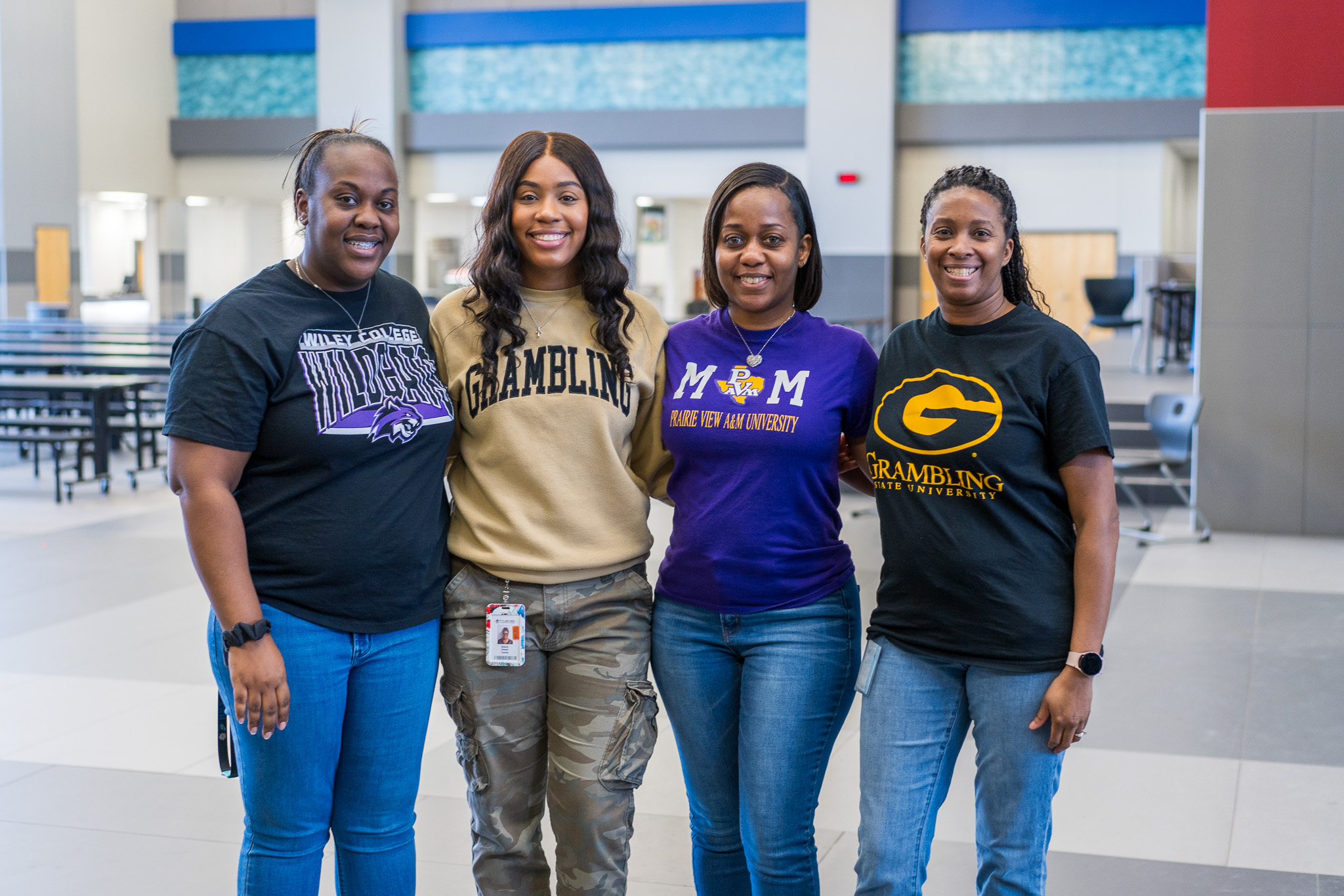 four African American women standing next to each other wearing college shirts