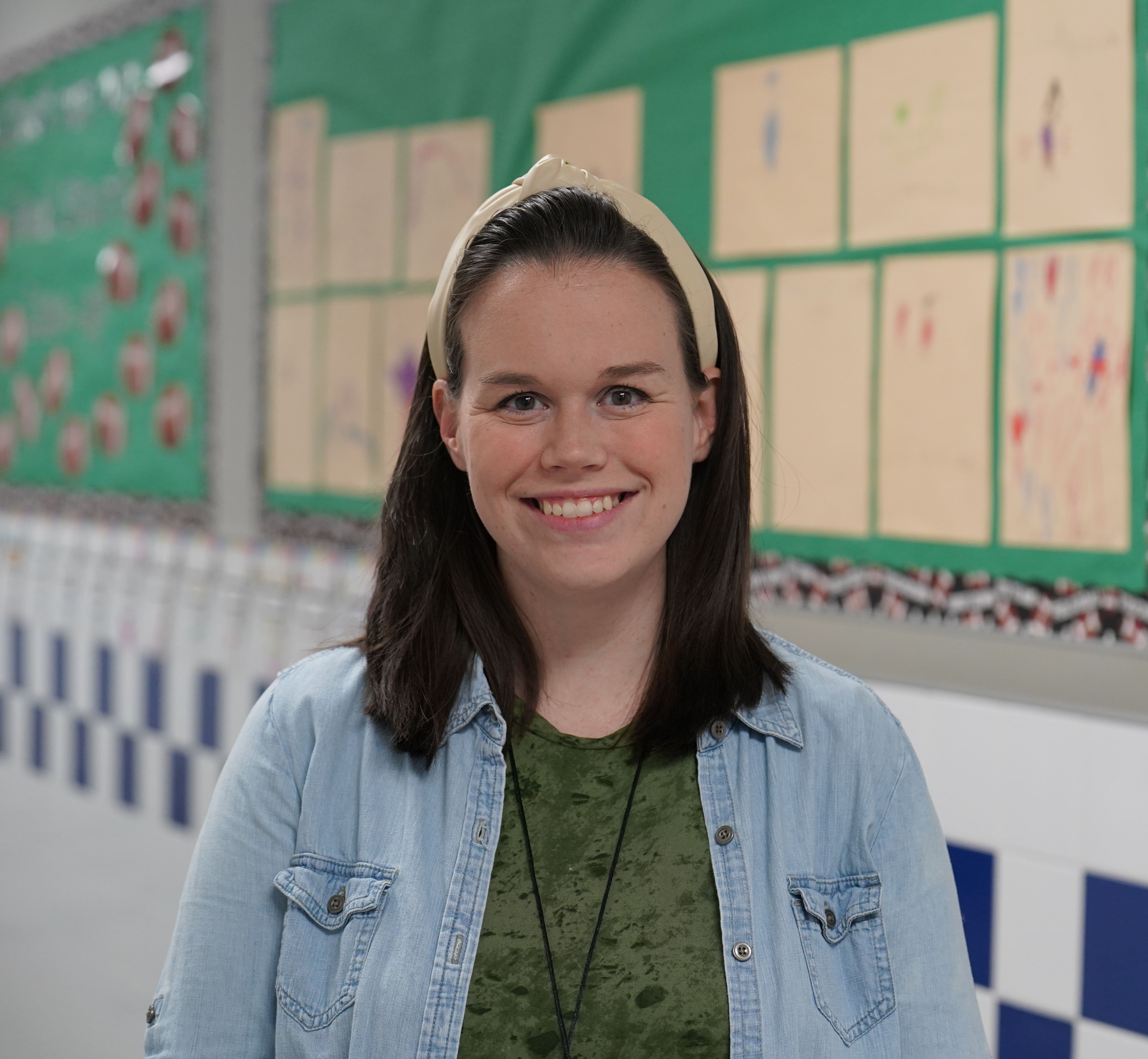 woman in a school hallway wearing a green shirt and denim shirt over it