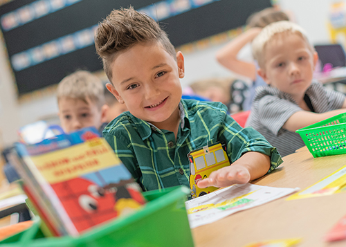 kindergarten age male student, hair spiked up, wearing a green shirt and sitting at a desk