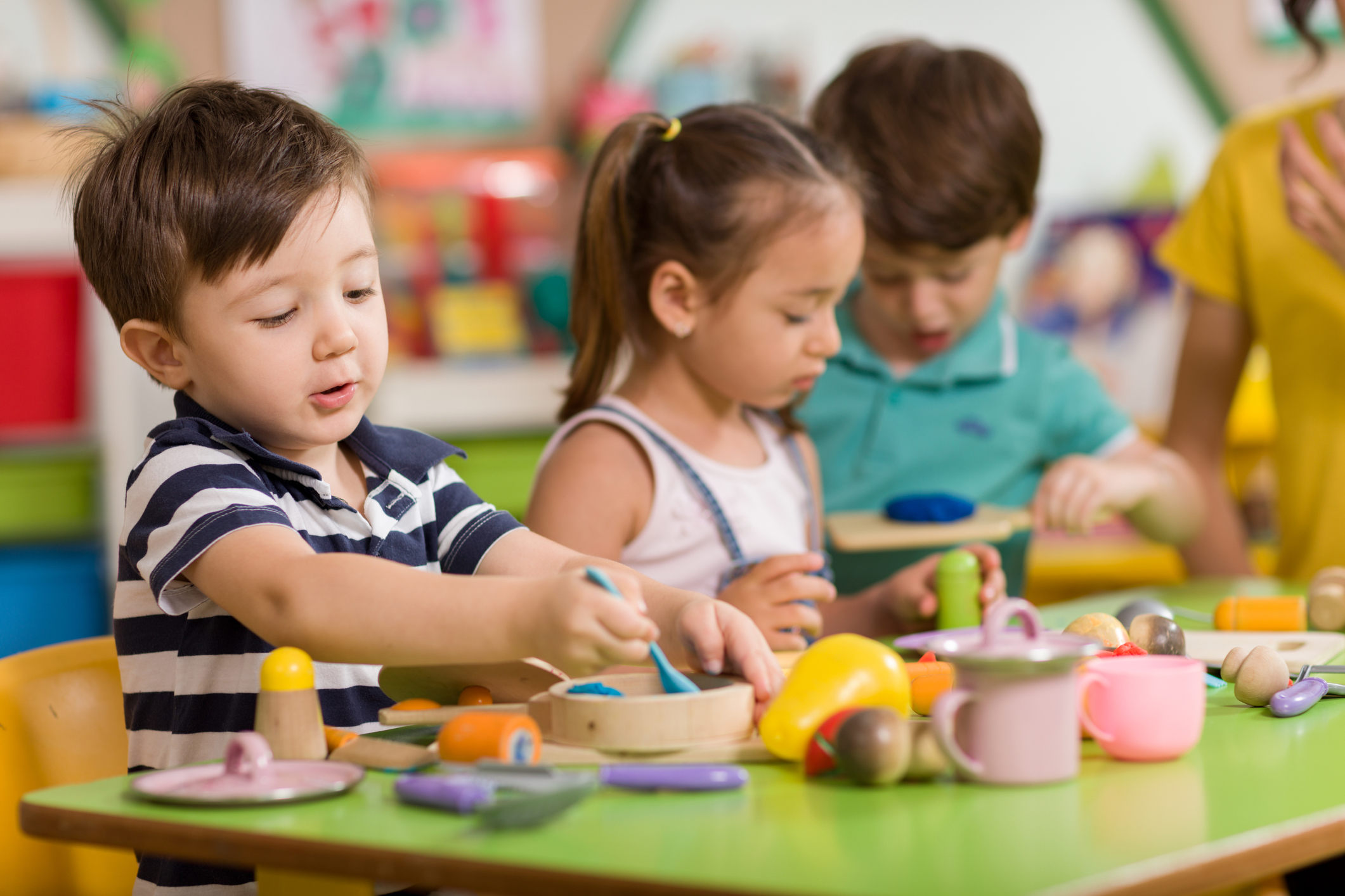 group of young male and female students sitting at the table playing with plastic food and dishes