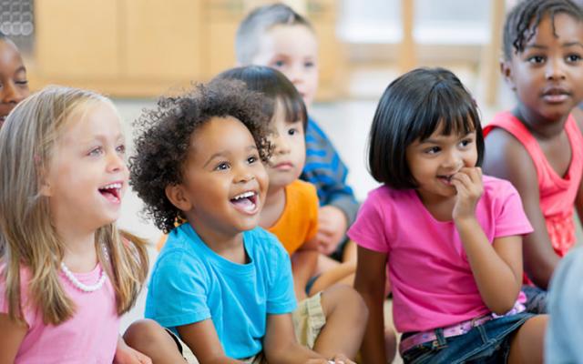 group of young students sitting on the floor in a classroom with big smiles on their faces