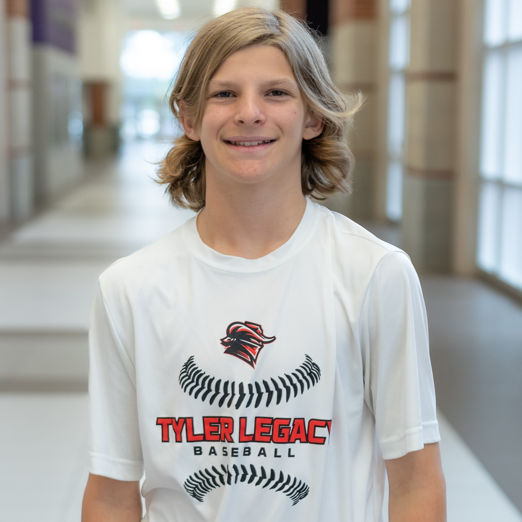 teen boy with long blond hair wearing a Tyler Legacy baseball t-shirt